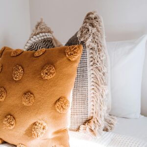 Comfortable colorful pillows placed on soft bed in light apartment illuminated by sunlight